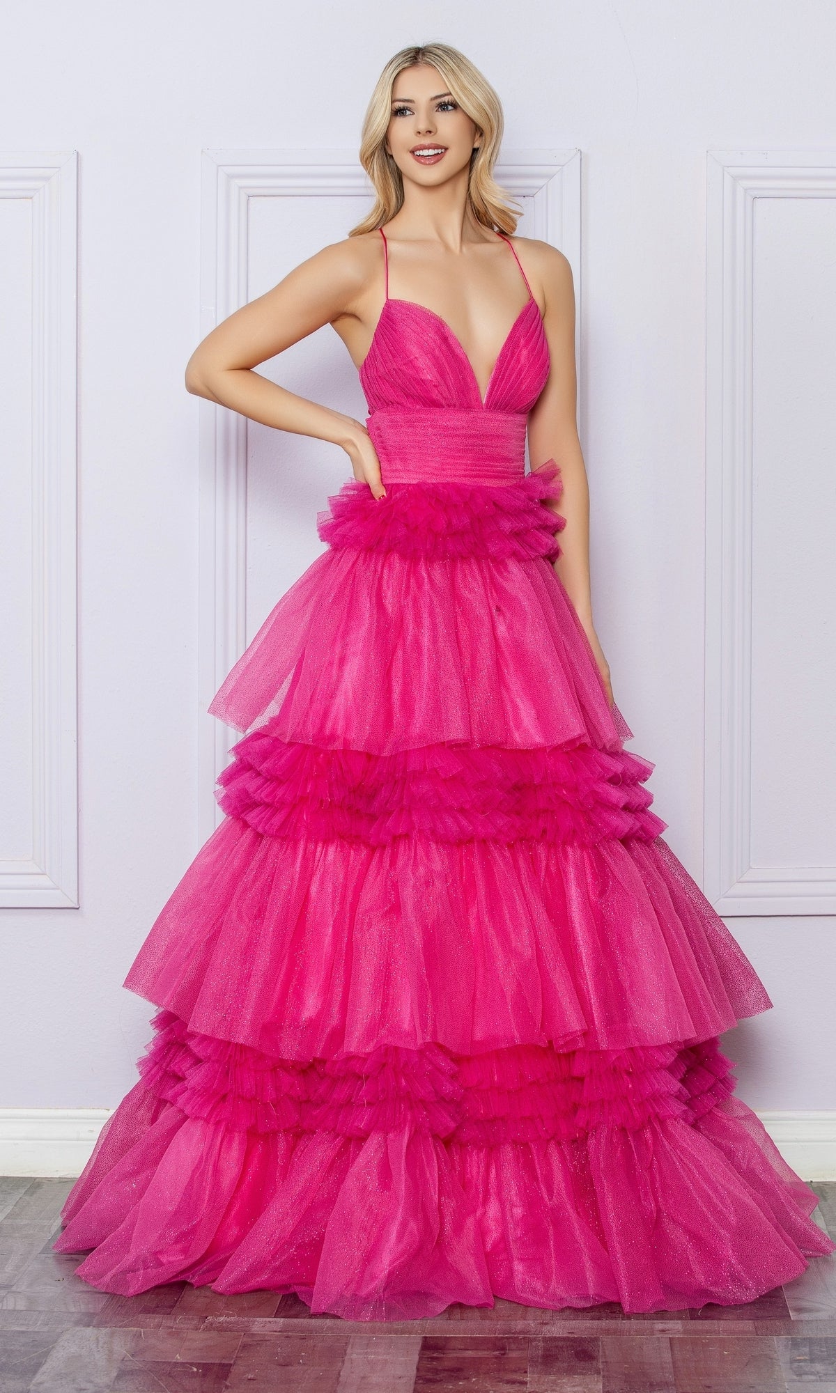 A woman wears the Nox Anabel Ruffled Glitter Prom Dress R1316, a vibrant hot pink tiered tulle gown with a deep V-neckline and spaghetti straps—perfect for making a grand entrance at any special occasion.
